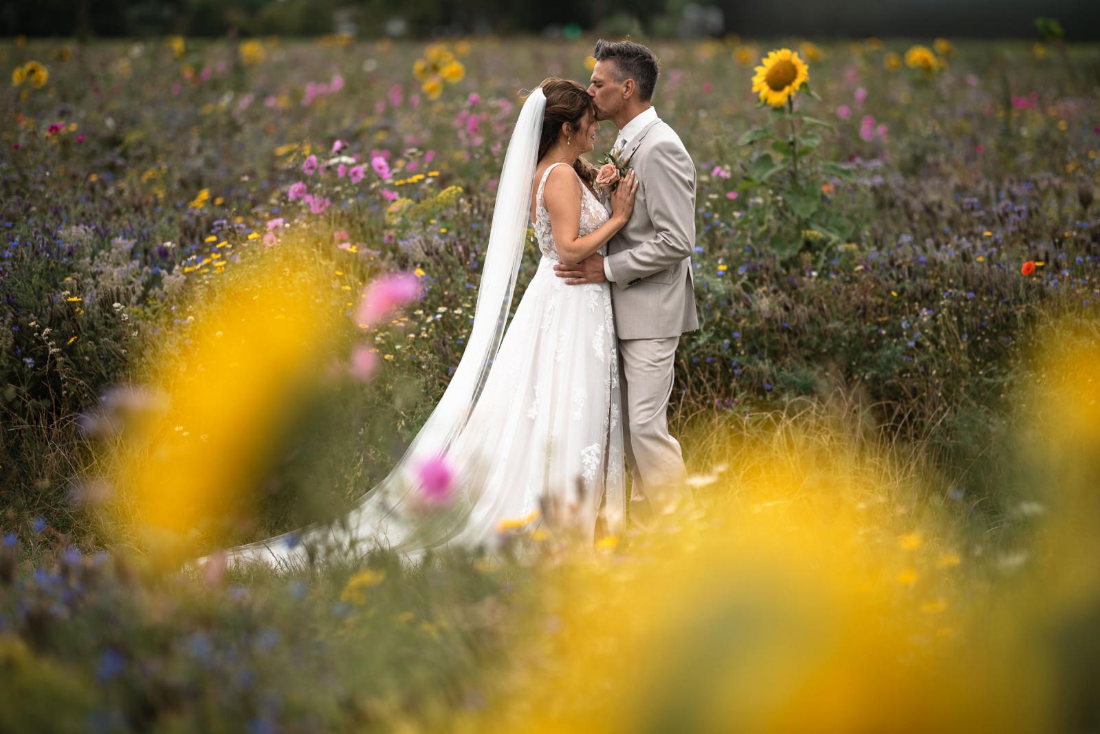 Intiem moment tussen Gerrit en Chantal, omringd door kleurrijke bloemen in een zomers veld.