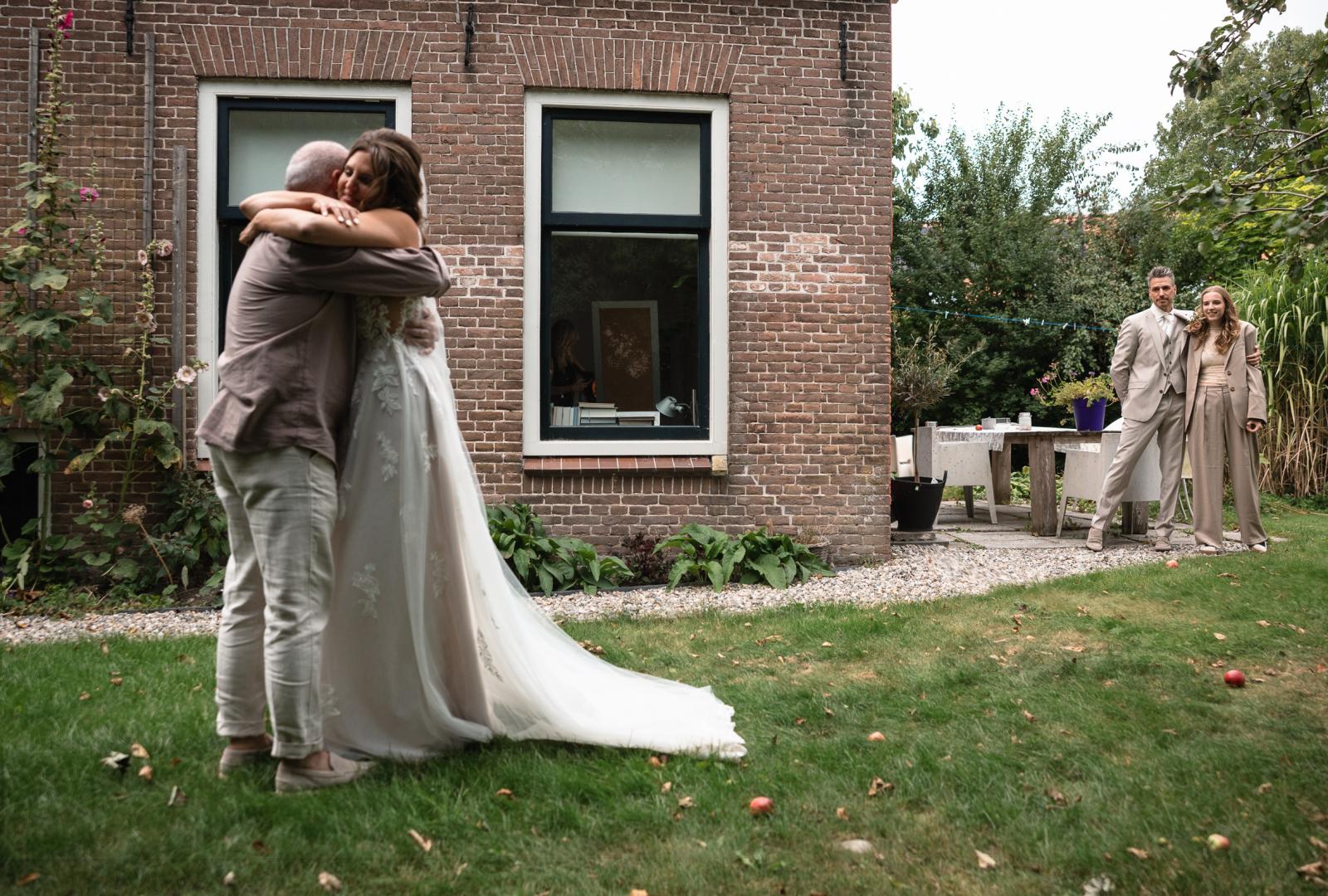 Ontroerende knuffel tussen vader en bruid, terwijl bruidegom en dochter toekijken.