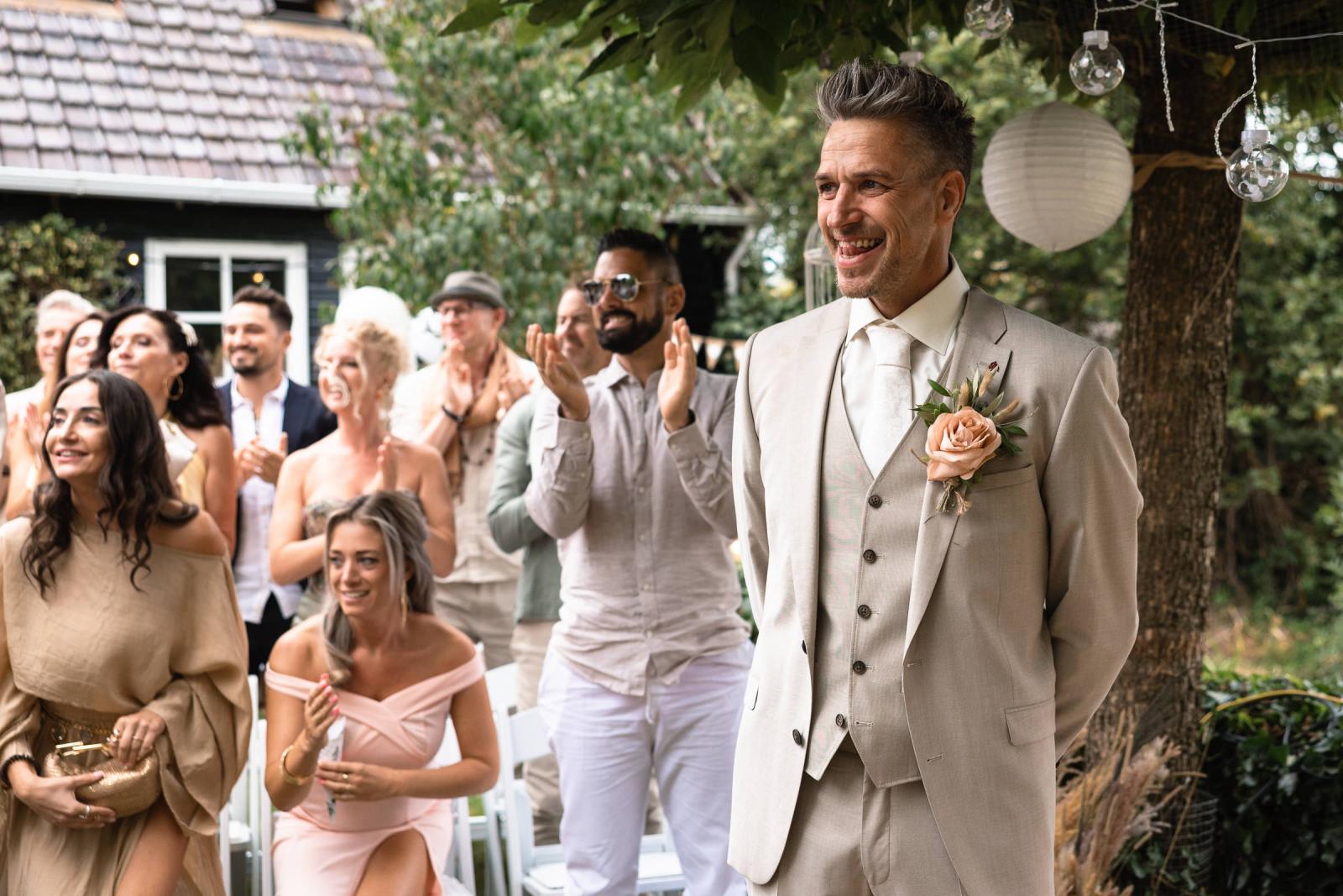Bruidegom ontroerd terwijl hij de bruid ziet binnenkomen, met gasten die applaudisseren.