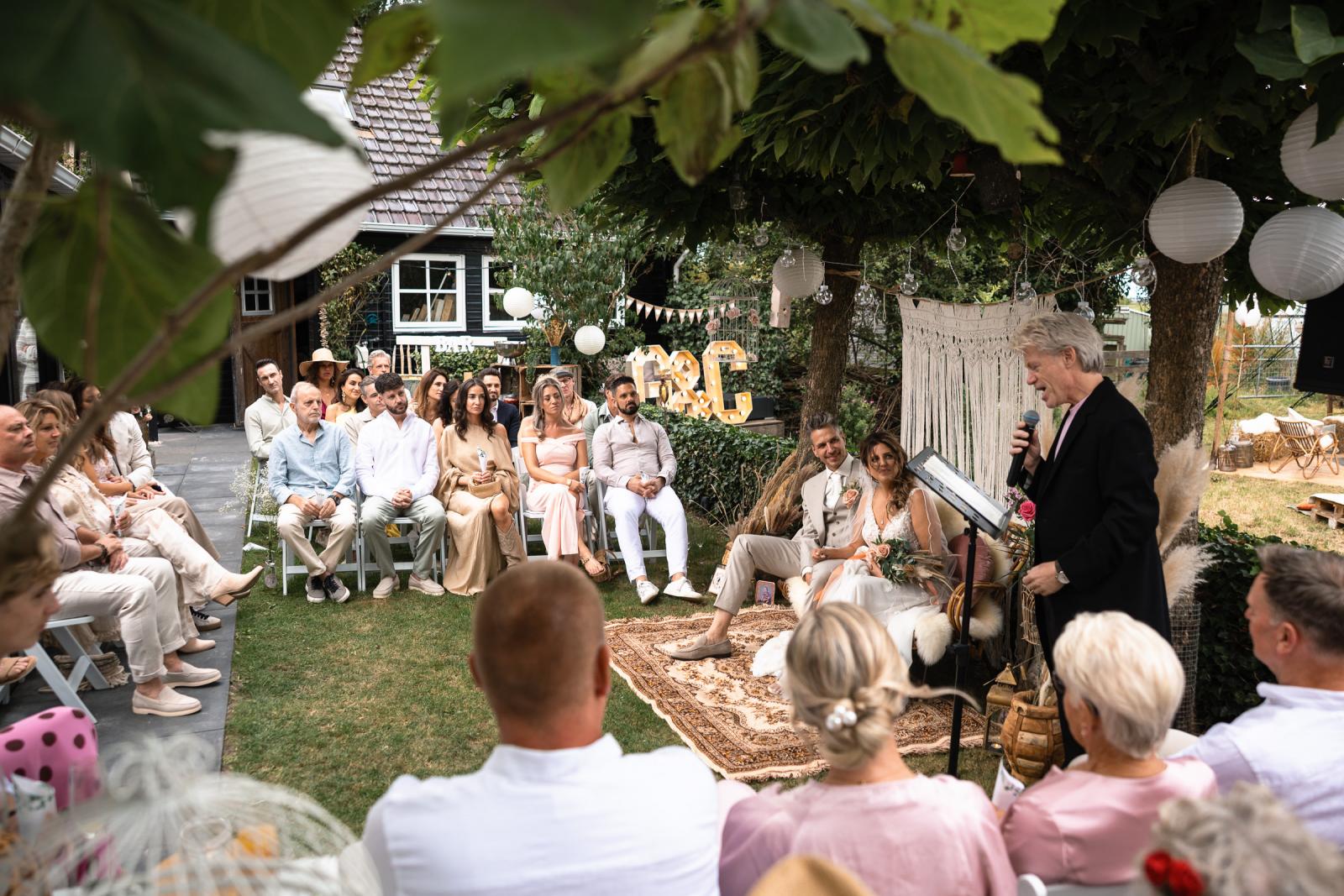 De trouwambtenaar spreekt tijdens de ceremonie, terwijl het bruidspaar en gasten aandachtig luisteren.