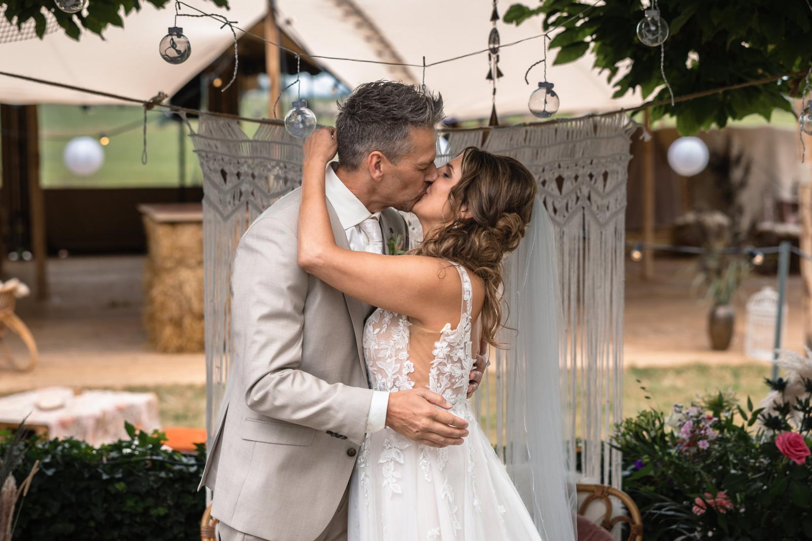 Het bruidspaar kust elkaar na het ja-woord, toegejuicht door gasten.