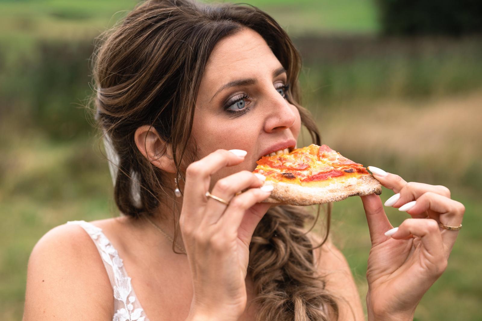 De bruid neemt een grote hap van een pizzapunt tijdens de trouwdag.
