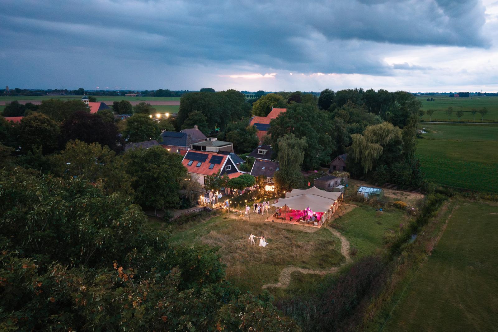 Sfeervolle avondlucht boven het dorp, met feesttent en verlichting bij de trouwlocatie.