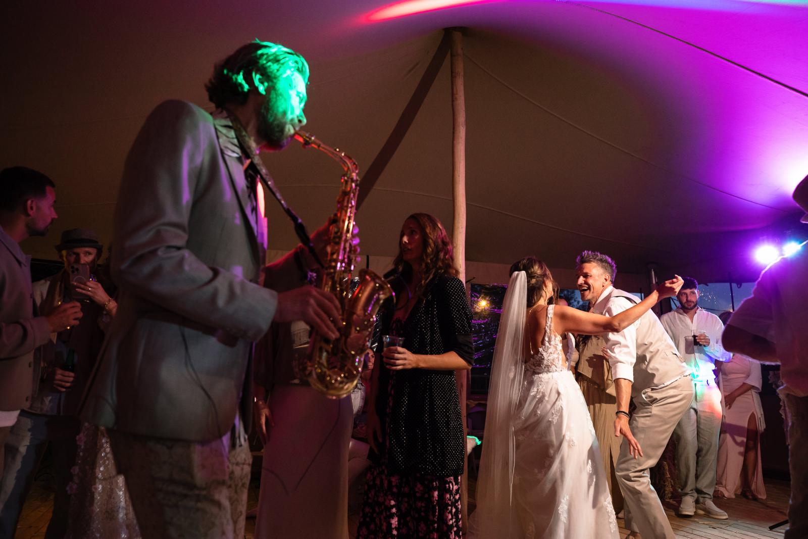 Het bruidspaar danst samen in de feesttent tijdens live saxophone, omringd door vrolijke gasten.
