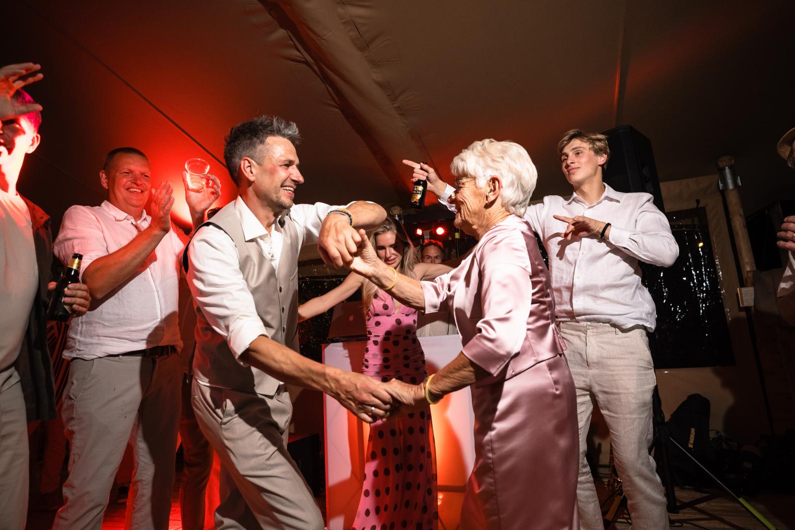 Oma danst met bruidegom en gasten feesten mee onder de sfeervolle verlichting in de tent.
