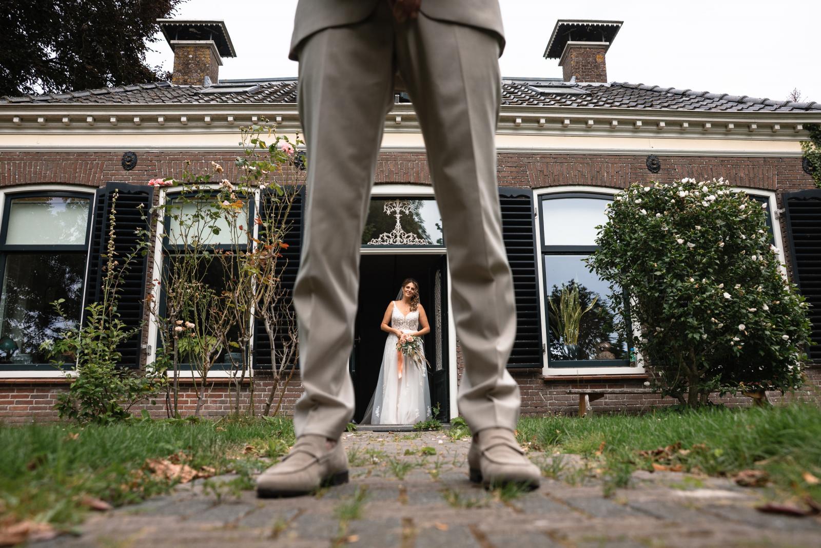 First look moment bij de voordeur – Chantal staat in haar trouwjurk terwijl Gerrit haar ophaalt.