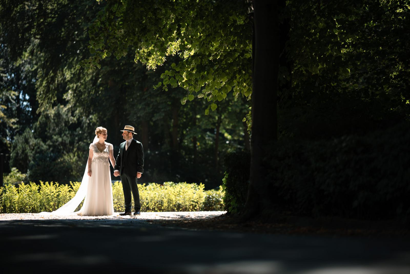 Bruidspaar Hanneke en Dennis wandelt hand in hand onder de bomen tijdens de bruidsreportage.