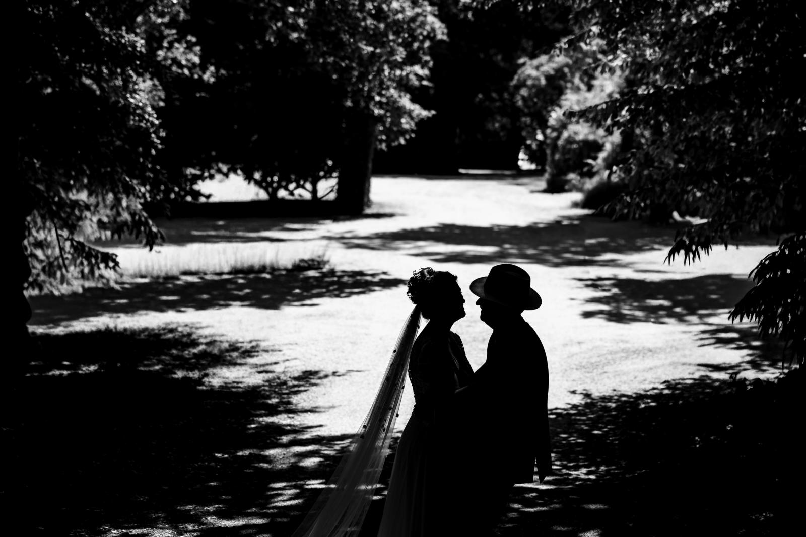 Zwart-wit silhouet van bruid Hanneke en bruidegom Dennis met hoed in het park.