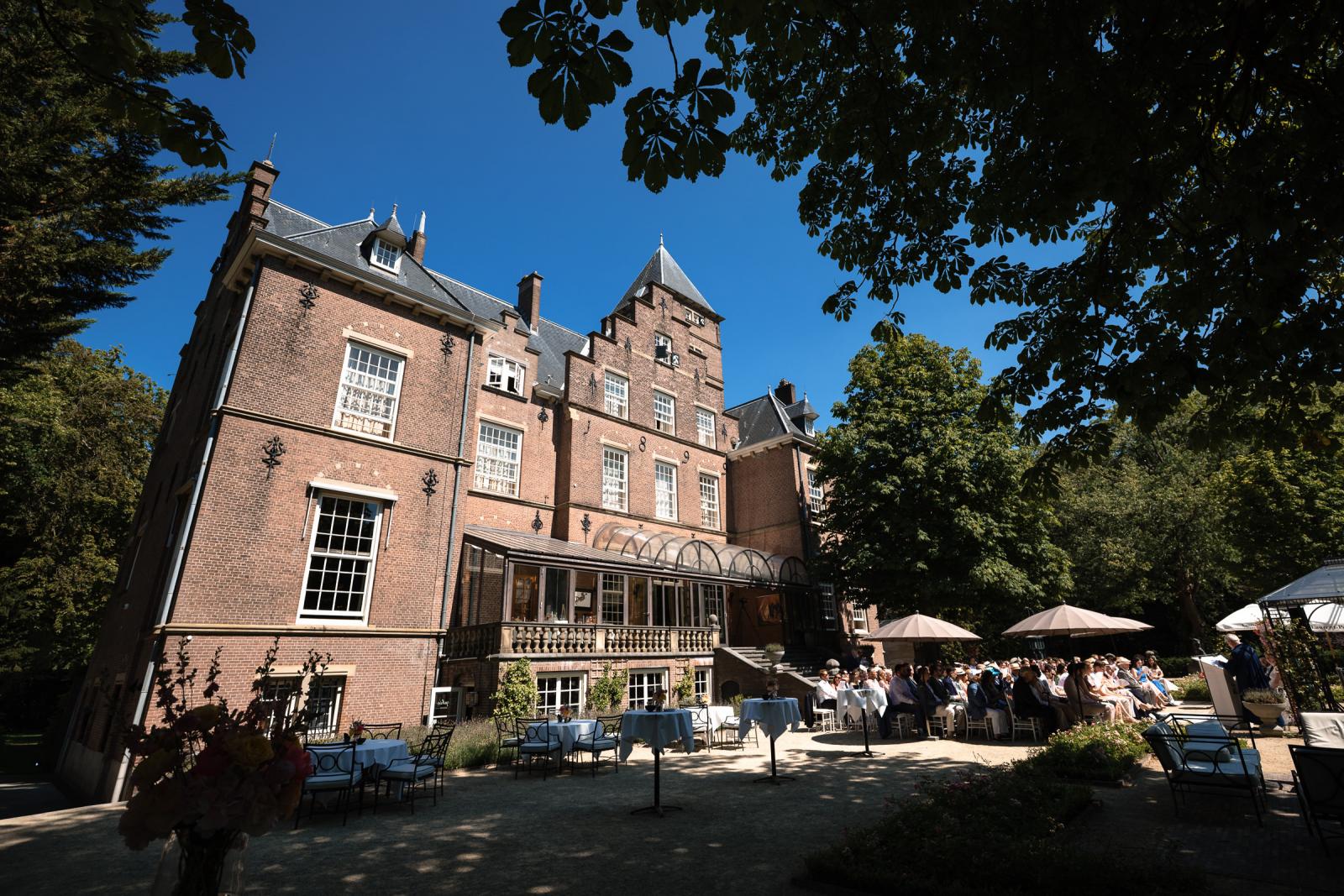 Overzicht van de zonnige huwelijksceremonie in de tuin van het historische landgoed.