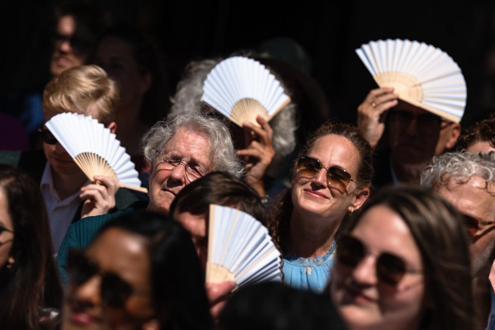 Bruiloftsgasten gebruiken witte waaier-waaiers tegen de zon tijdens de ceremonie.