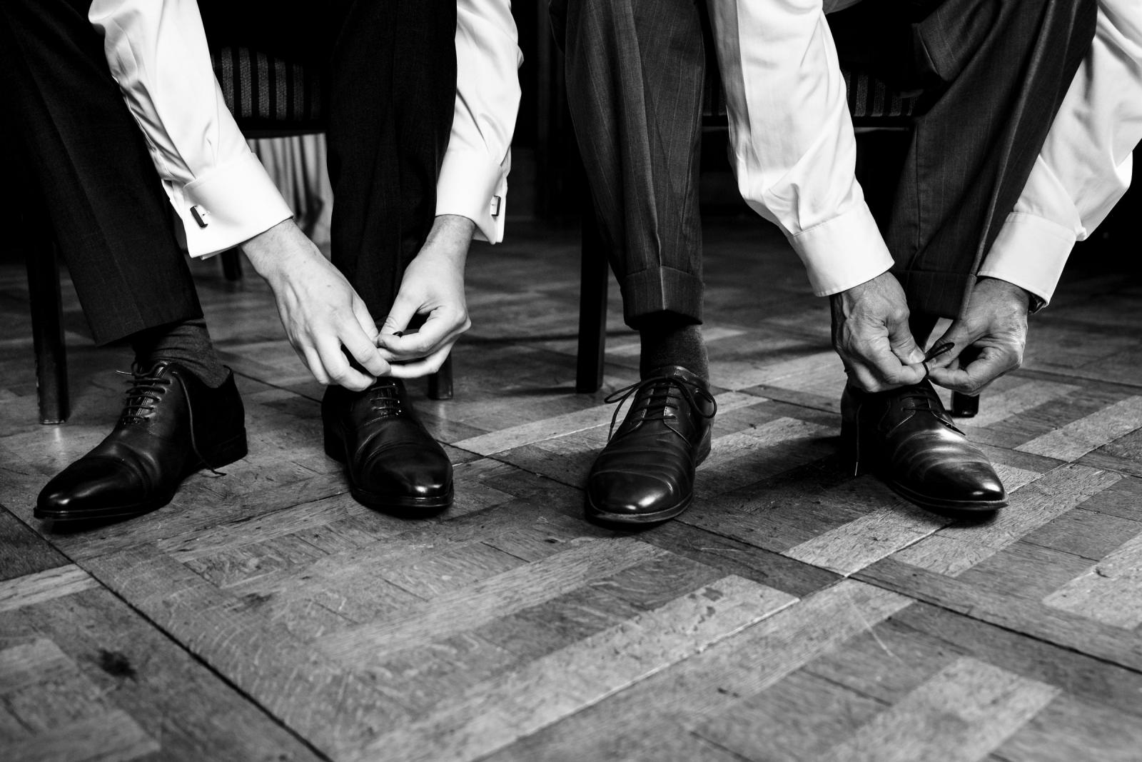 Bruidegom en gast strikken hun zwarte trouwschoenen voor de bruiloft op de houten vloer.