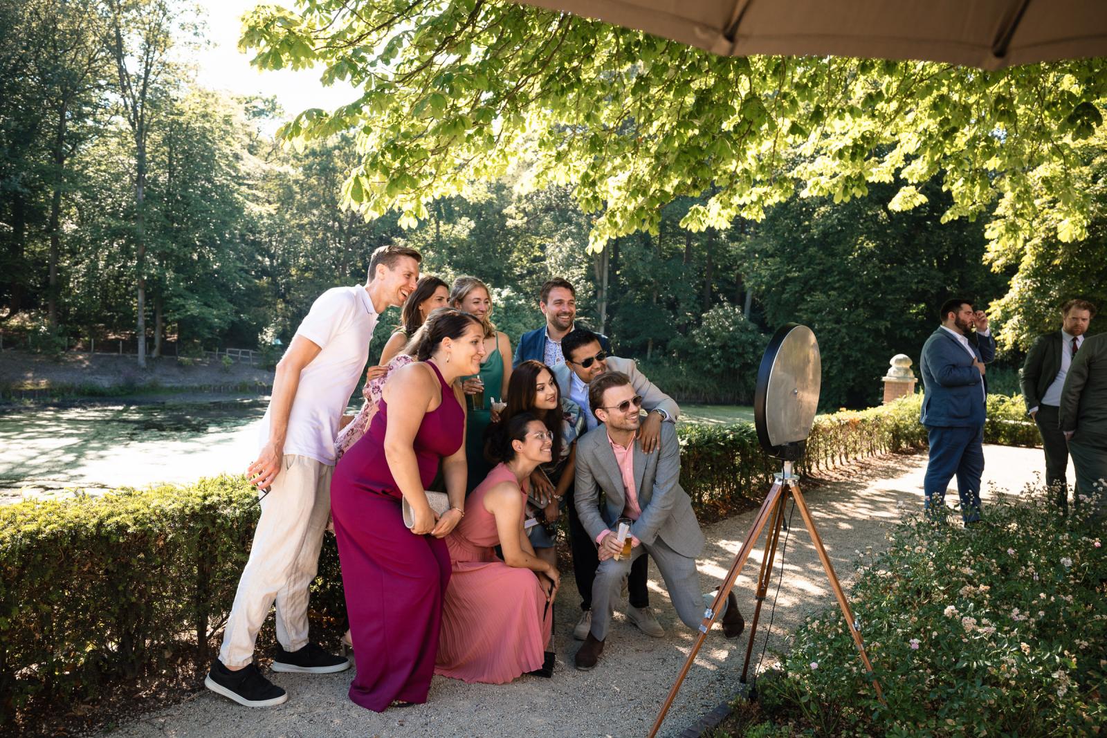 Vrolijke bruiloftsgasten maken samen een foto bij een photobooth in de kasteeltuin.
