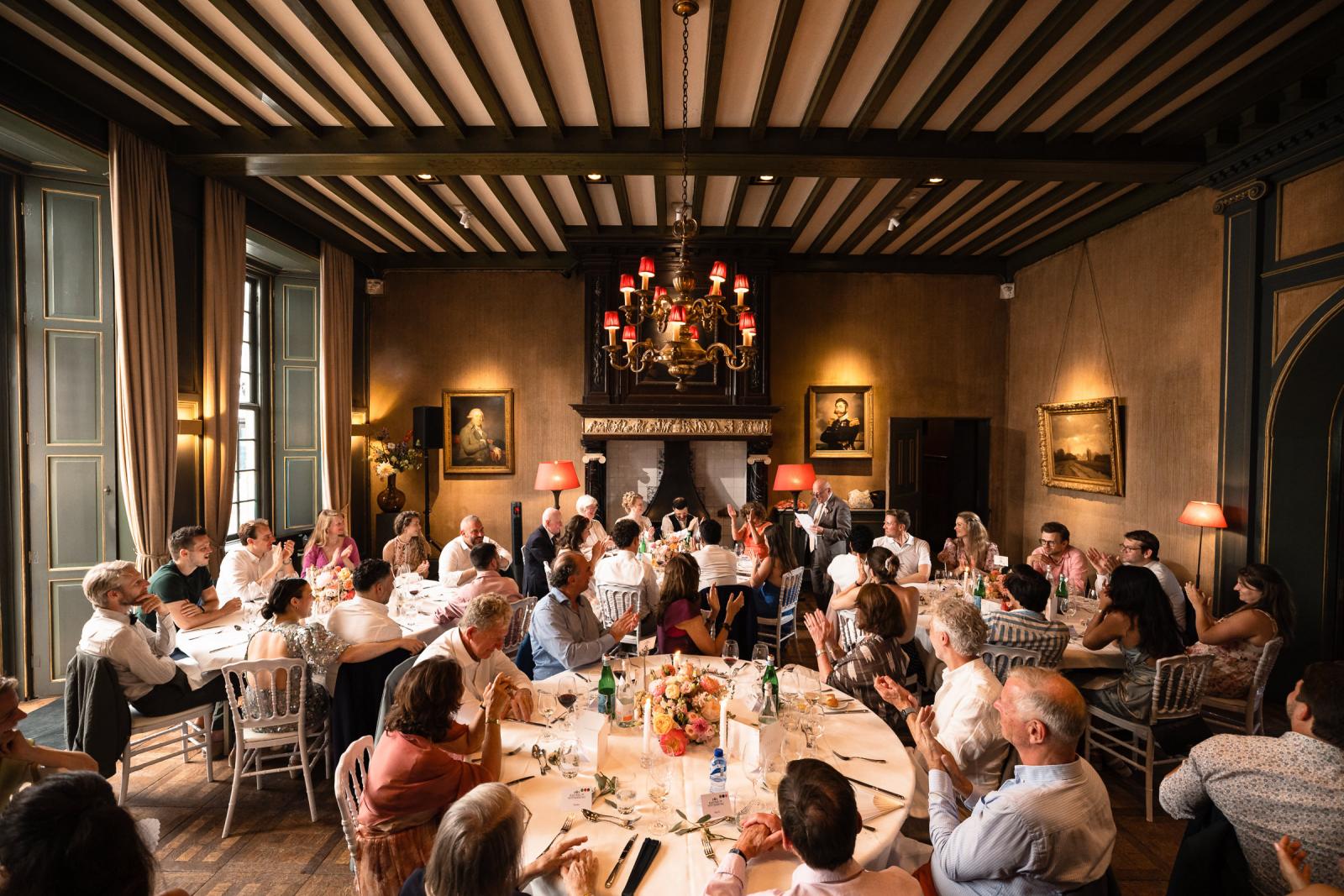 Sfeervol diner met proost moment van het bruidspaar en hun gasten in de klassieke diner zaal met een grote kroonluchter .