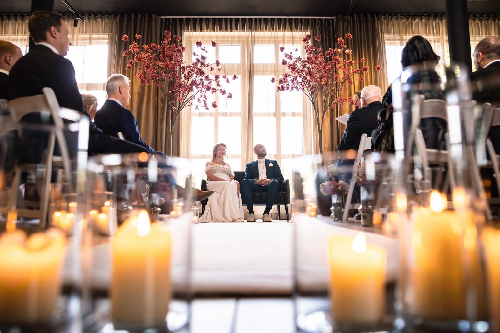 Een uniek sfeerbeeld van de ceremonie, gefotografeerd door een 'veld' van brandende kaarsen op de grond, met de focus op het bruidspaar Judith en Mark.