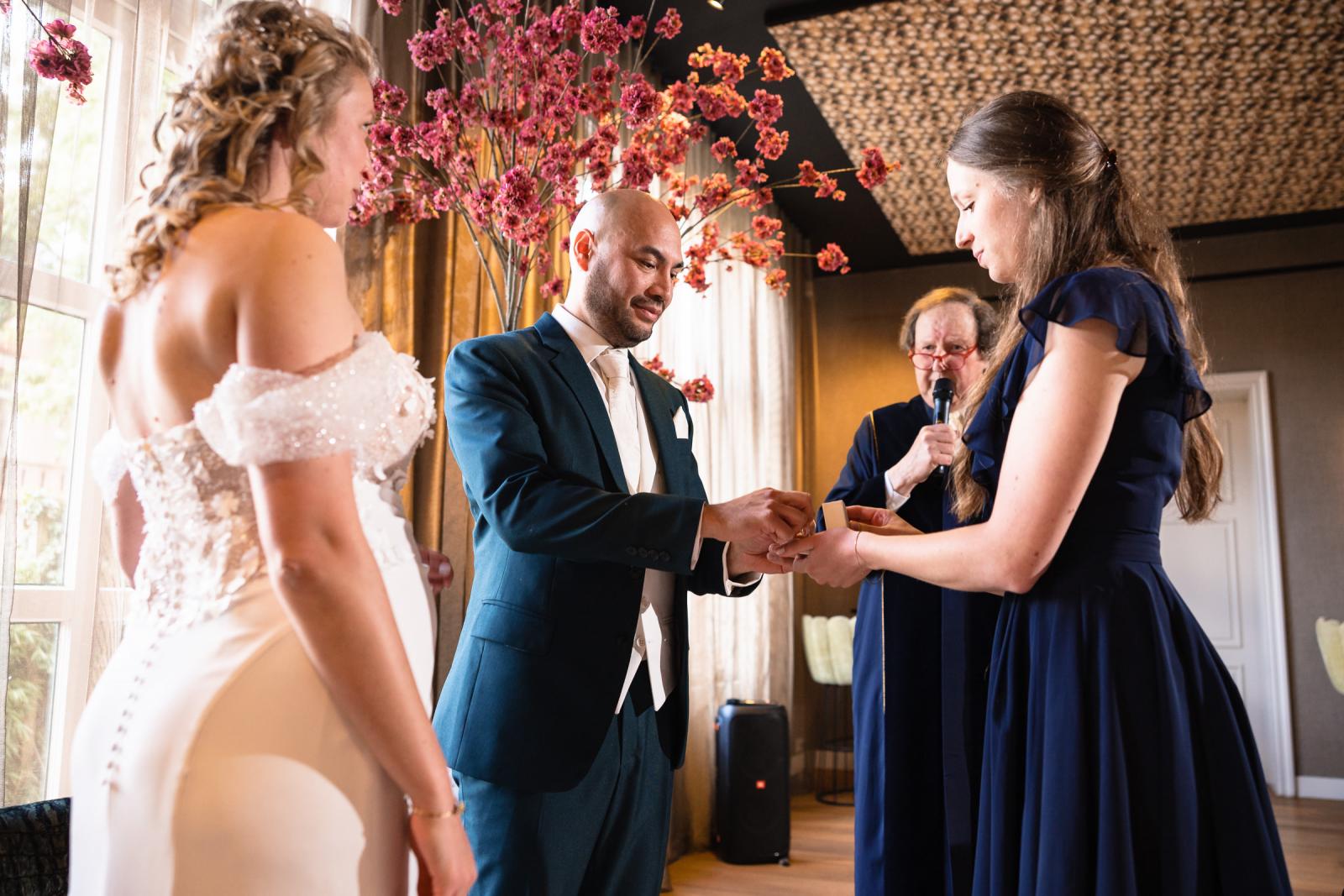 Een close-up van de ringenoverdracht: bruidegom Mark en een getuige overhandigen de trouwringen in een houten doosje aan de ambtenaar.