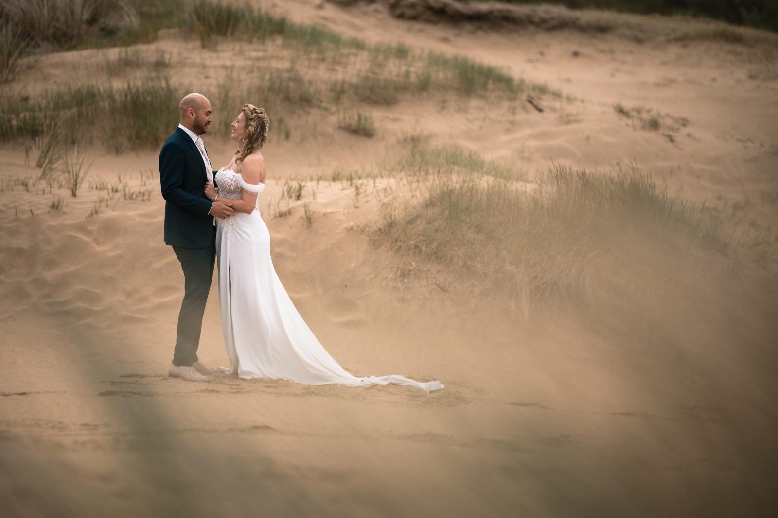 Romantisch portret van Judith en Mark die elkaar teder vasthouden tijdens de firstlook en aankijken in het duinlandschap.