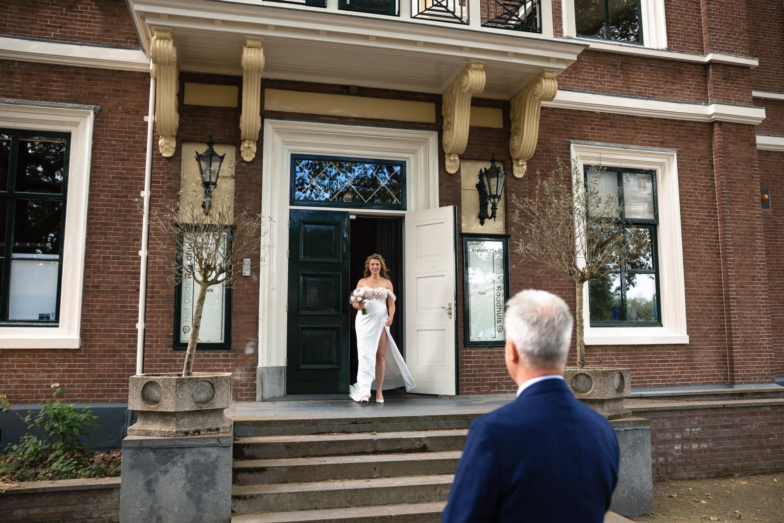 Bruid Judith stapt met haar trouwboeket naar buiten bij Het Oude Raadhuis voor de first look met haar vader.