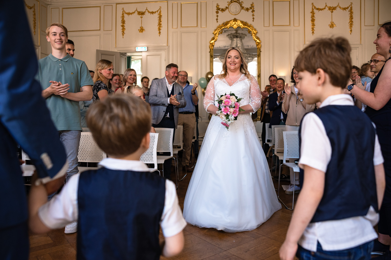 Bruid loopt naar bruidegom en twee kinderen toe voor haar ceremonie opkomst Trouwfotograaf Spaansche Hof Den Haag