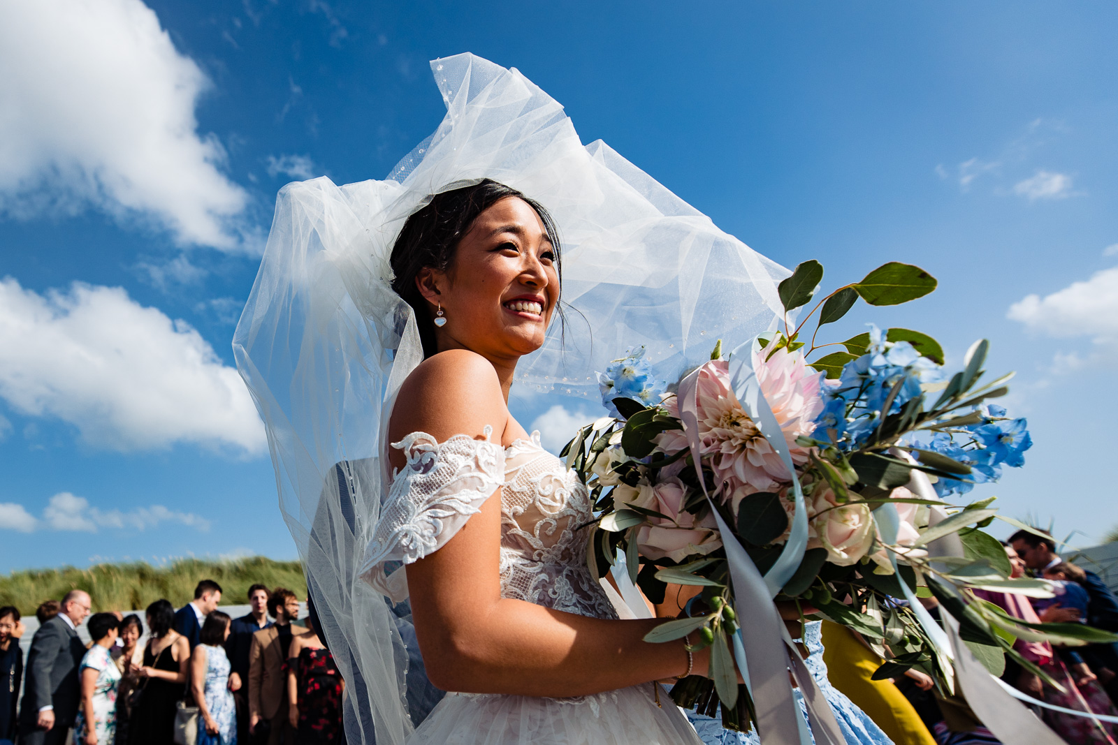 de wind speelt met de sluier van deze prachtige chinese bruid tijdens groepgsfoto's
