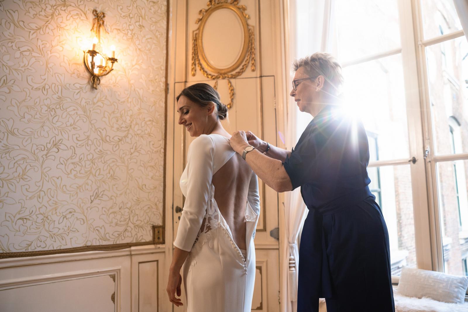 Bruid wordt geholpen met haar trouwjurk in stijlvolle suite bij Het Spaansche Hof Den Haag – voorbereiding bruiloft.