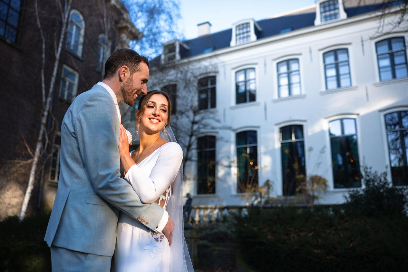 Bruidspaar poseert liefdevol voor de witte gevel van Het Spaansche Hof – stijlvolle trouwfoto Den Haag.