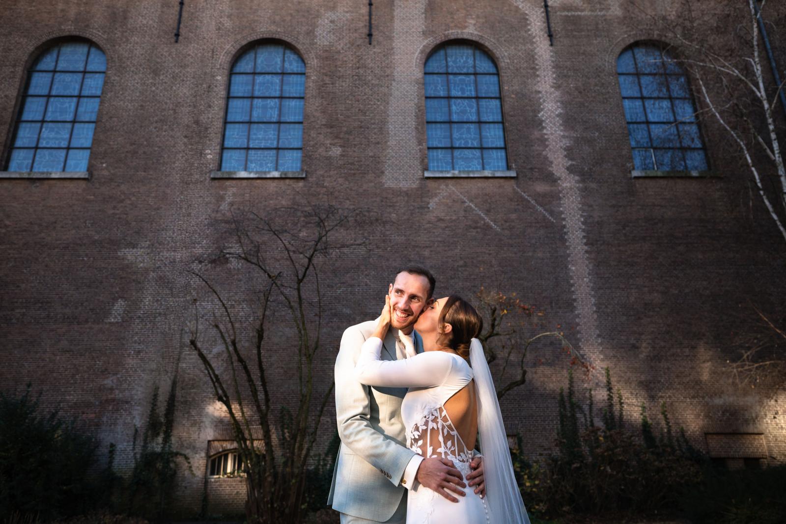 Bruid kust bruidegom voor karakteristieke bakstenen muur – spontane trouwfoto Spaansche Hof Den Haag.