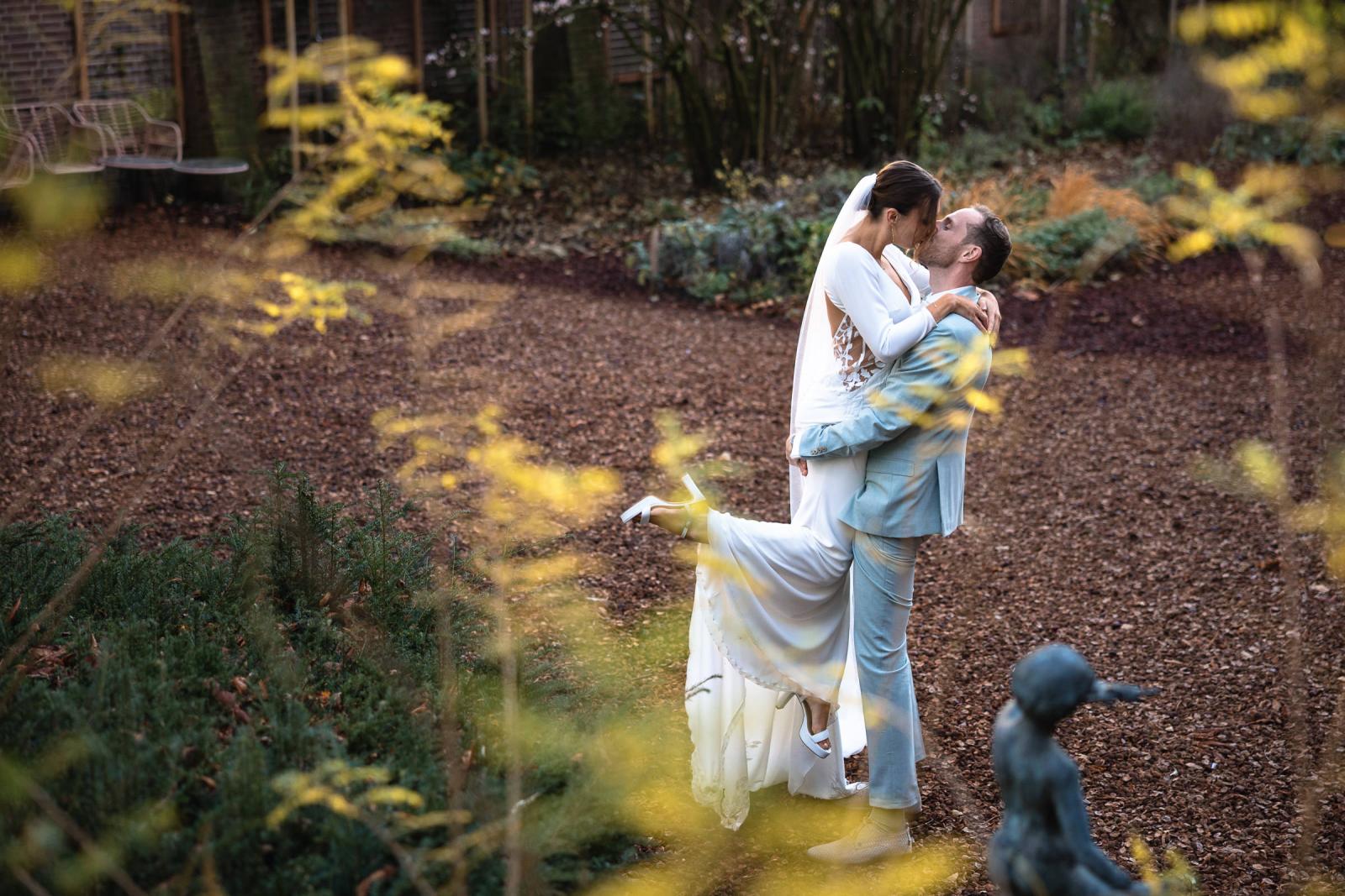 Bruidegom tilt bruid op tijdens fotoshoot in tuin Spaansche Hof Den Haag – speels trouwmoment.