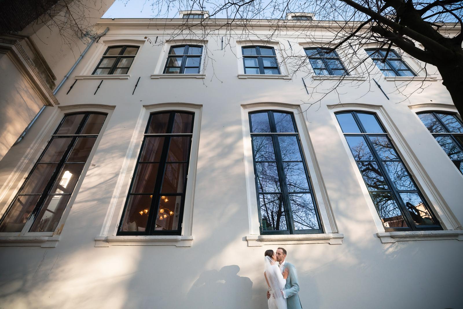 Bruidspaar poseert onder hoge ramen van Het Spaansche Hof – architectuur en bruidsfotografie Den Haag.