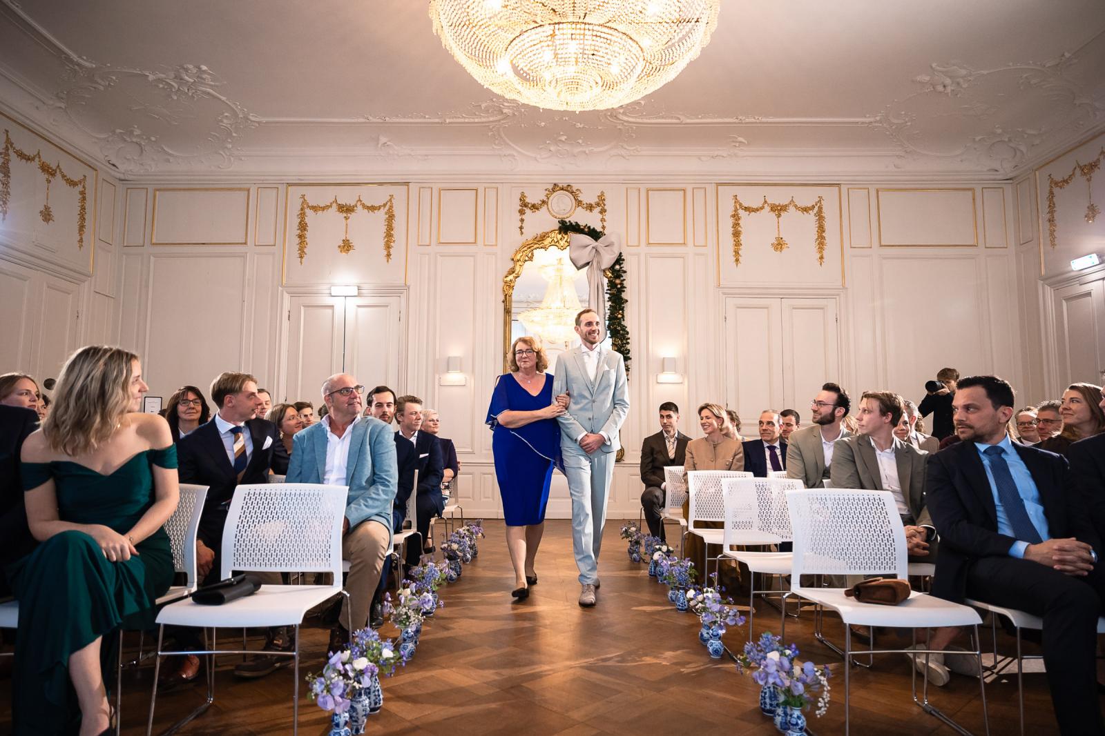 Bruidegom loopt samen met moeder het gangpad op – binnenkomst ceremonie Spaansche Hof Den Haag.