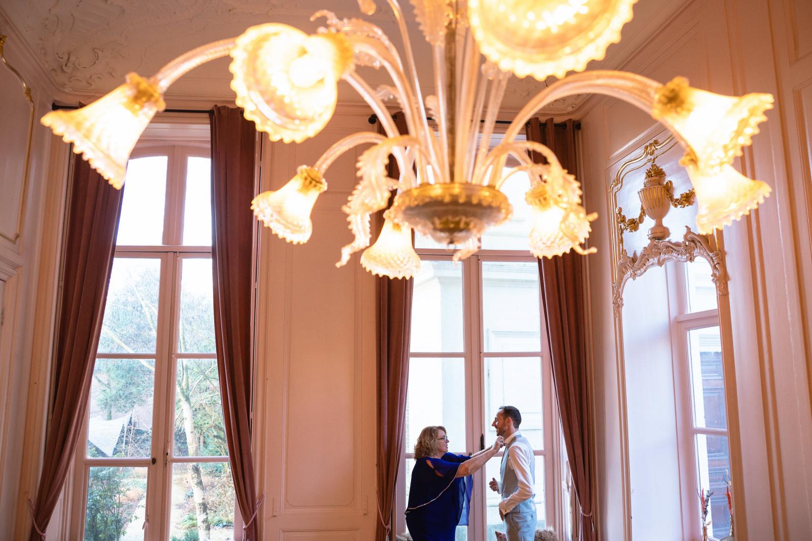 Bruidegom krijgt hulp met zijn das in een elegante kamer van Het Spaansche Hof Den Haag – voorbereidingen bruiloftsfotografie.