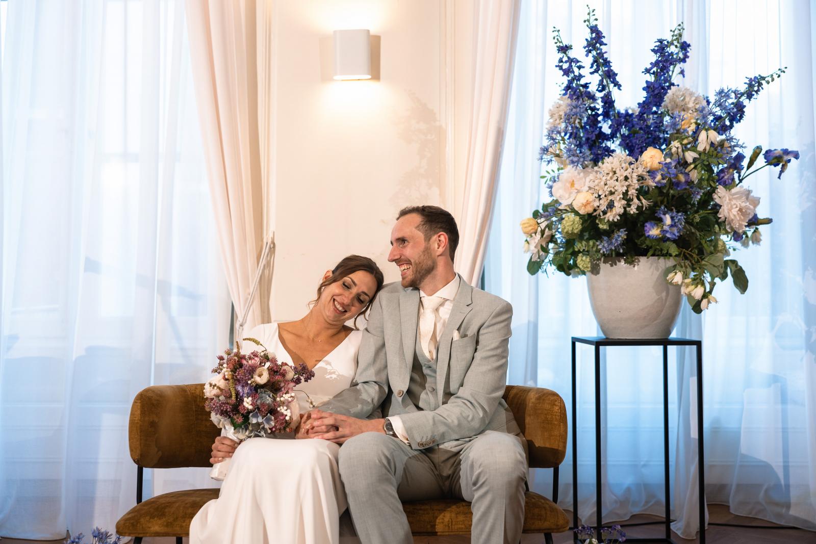 Bruidspaar zit ontspannen samen, omringd door bloemen – liefdevolle sfeer Spaansche Hof Den Haag.