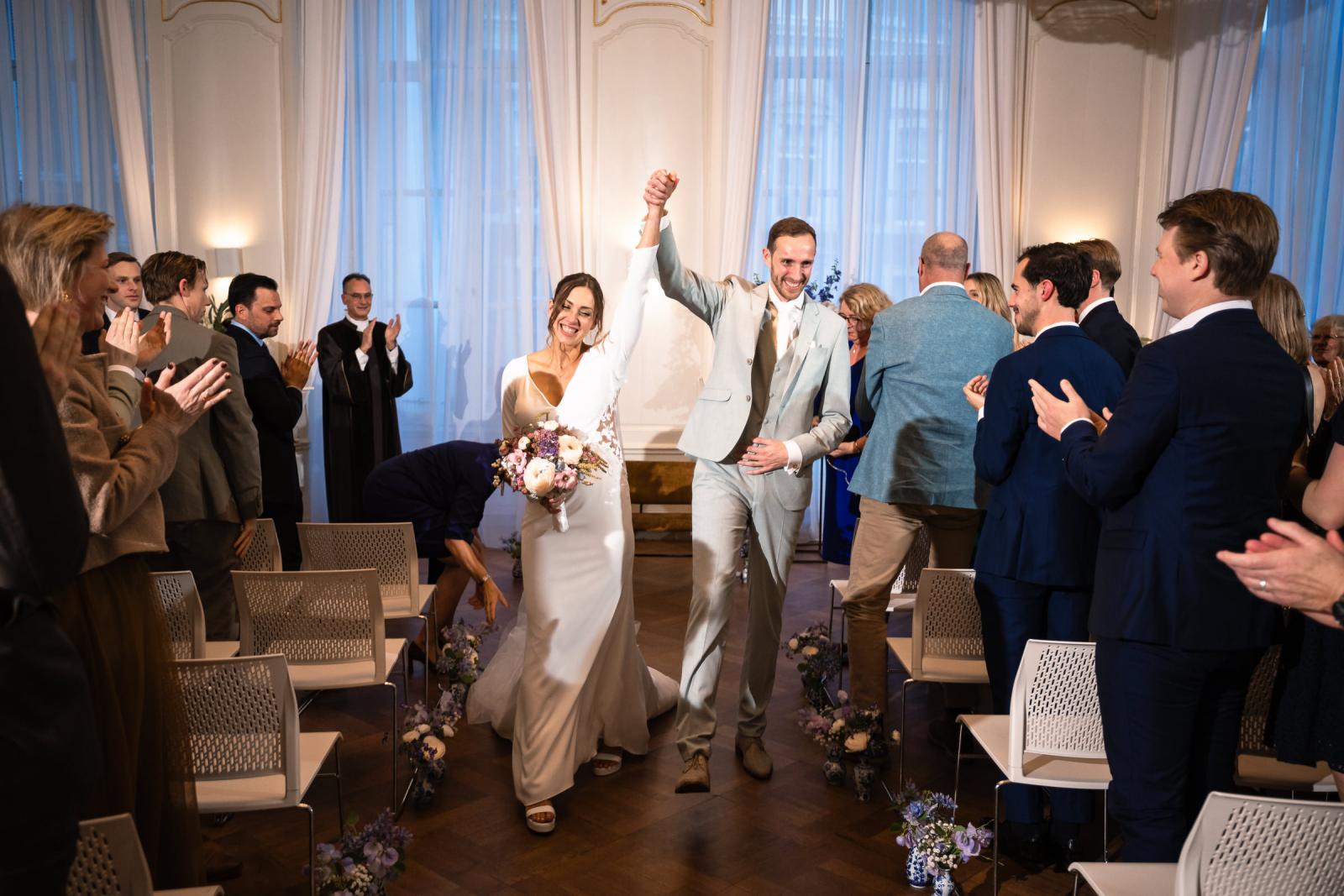 Bruidspaar loopt juichend de zaal uit na de ceremonie – feestelijke afsluiting Spaansche Hof Den Haag.