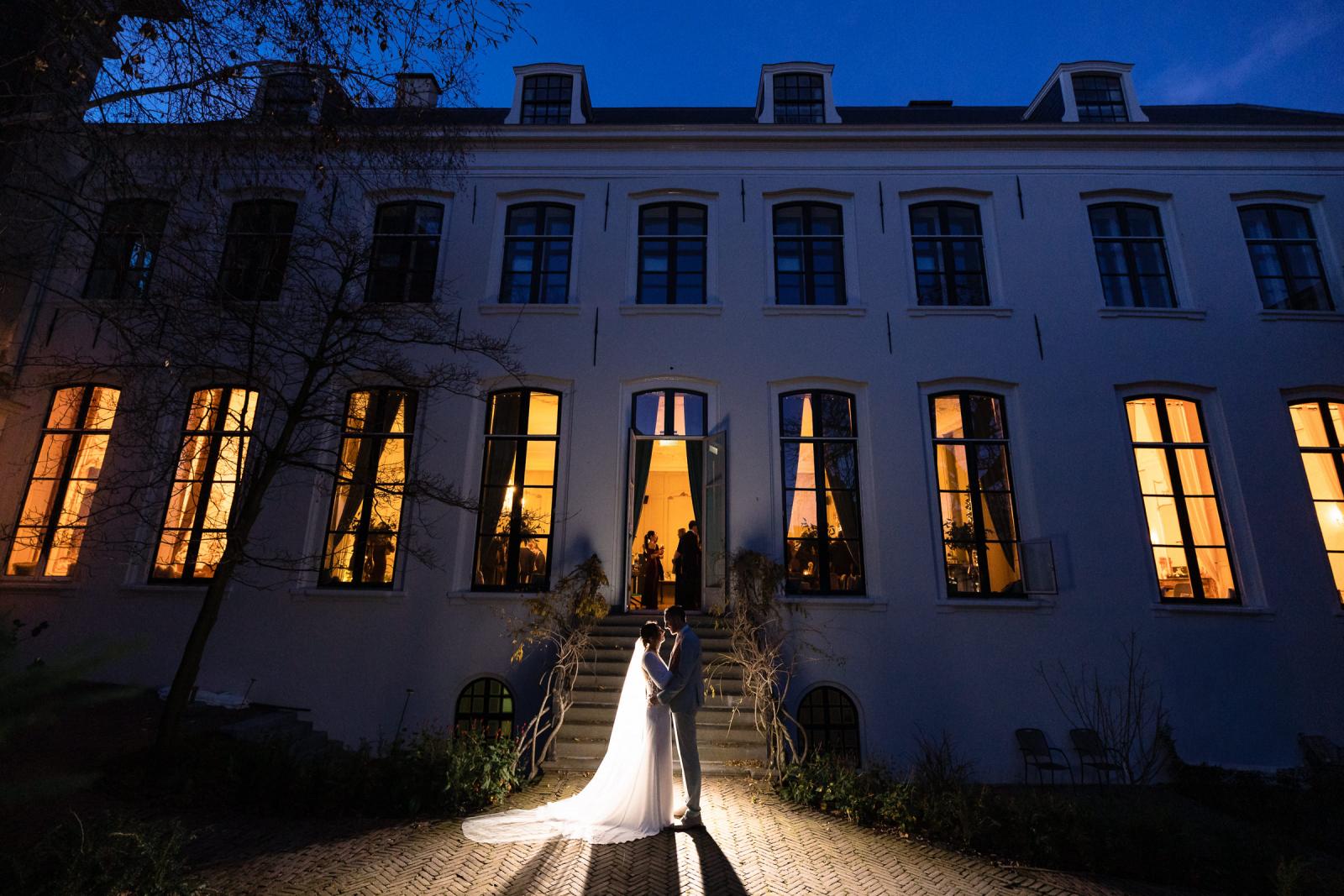 Avondportret van bruidspaar voor verlicht Spaansche Hof – romantische trouwfoto Den Haag.
