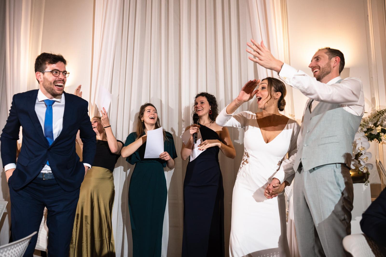Bruidspaar en vrienden zingen samen tijdens avondprogramma – feestelijke bruiloft Spaansche Hof Den Haag.