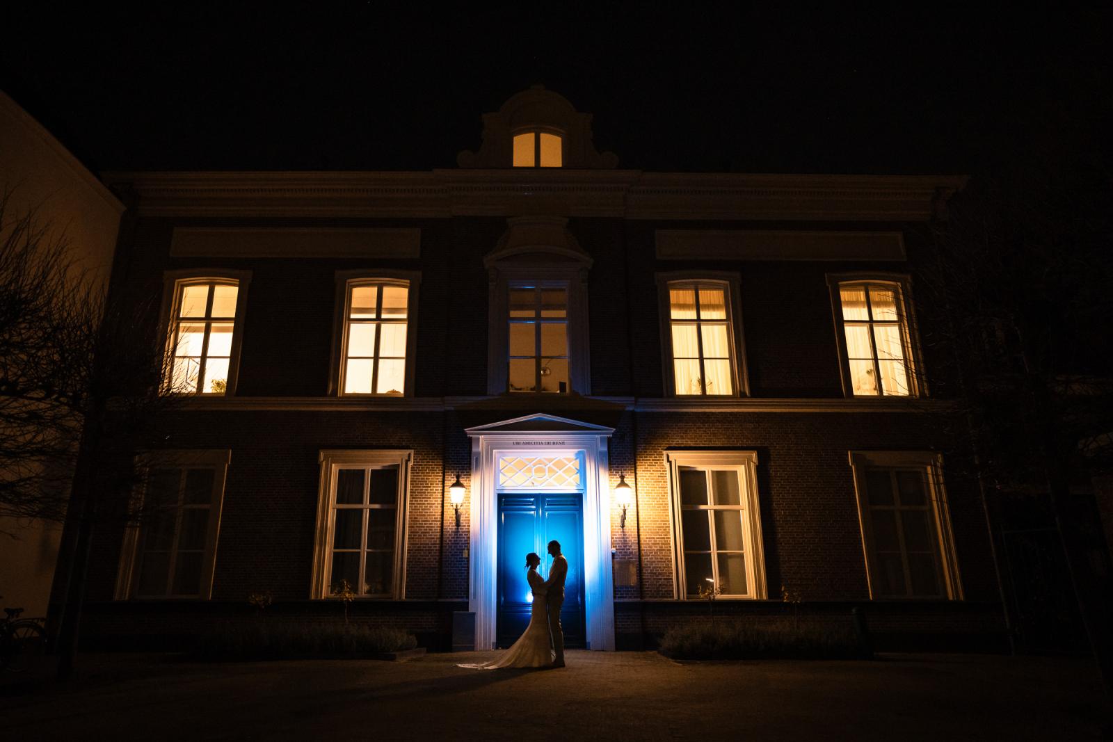 Bruidspaar verlicht in de nacht bij entree Spaansche Hof – sfeervolle afsluiter trouwreportage Den Haag.