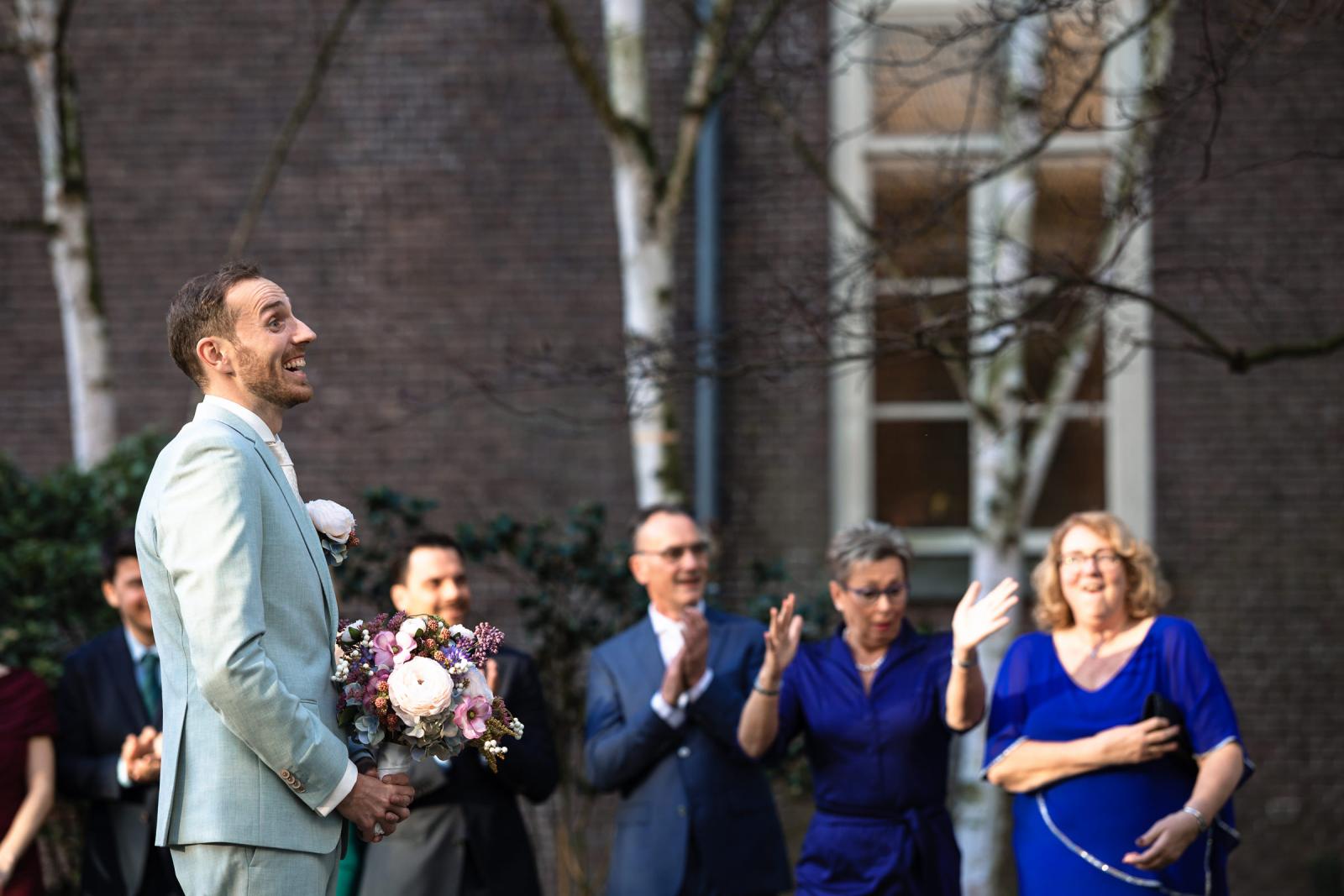 Bruidegom wacht gespannen buiten met bruidsboeket – first look moment Spaansche Hof Den Haag.
