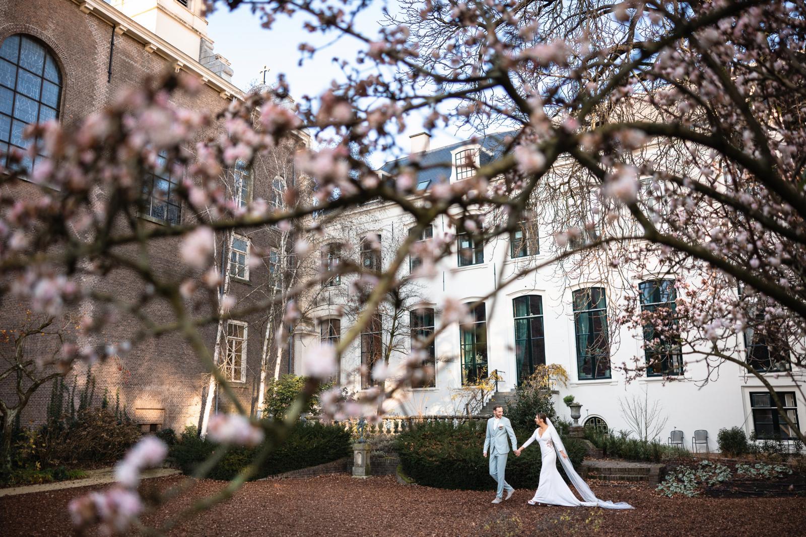 Bruid en bruidegom wandelen hand in hand door de romantische tuin van Het Spaansche Hof Den Haag.