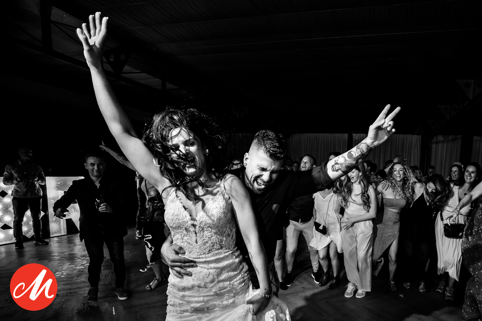 Energiek zwart-wit beeld van een dansende bruid en bruidegom met de handen in de lucht tijdens de feestavond van een bruiloft.