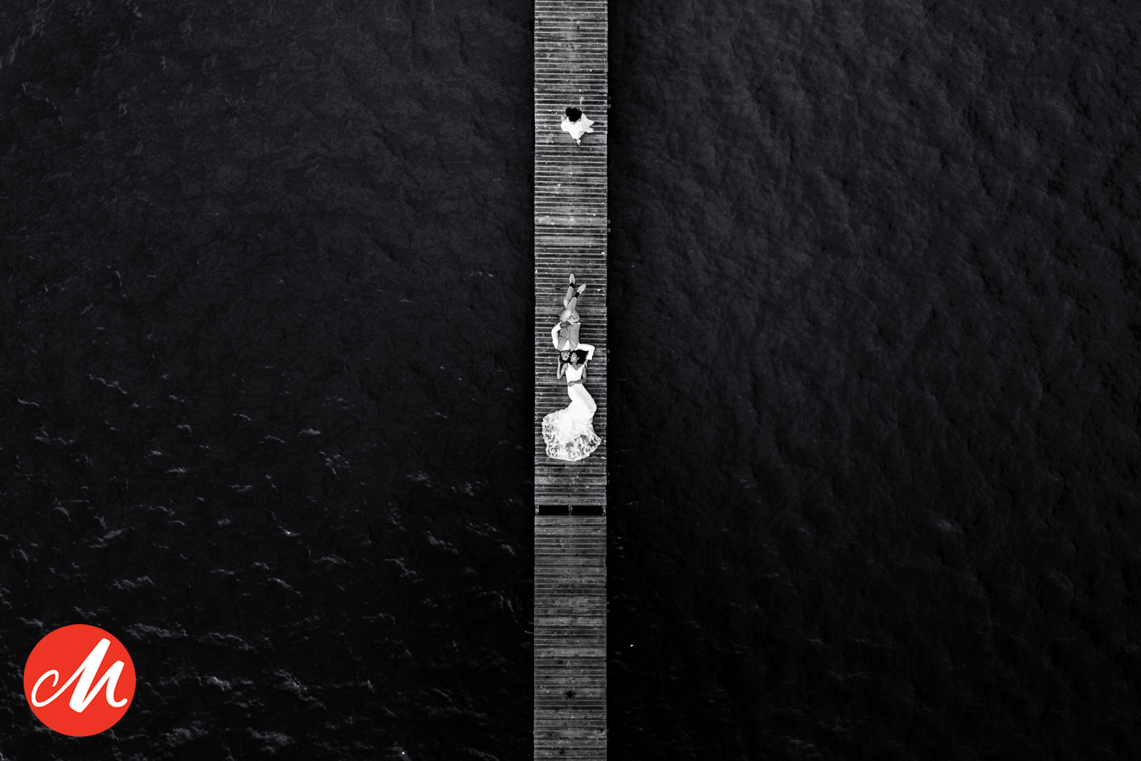 Luchtfoto van een bruidspaar dat samen op een houten steiger aan het water ligt, minimalistische bruidsfotografie door Paco van Leeuwen.