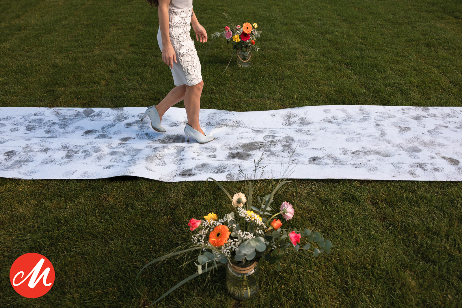 Detailfoto van een loper met modderige voetstappen op het gras tijdens een buitenbruiloft, journalistieke trouwfotografie.
