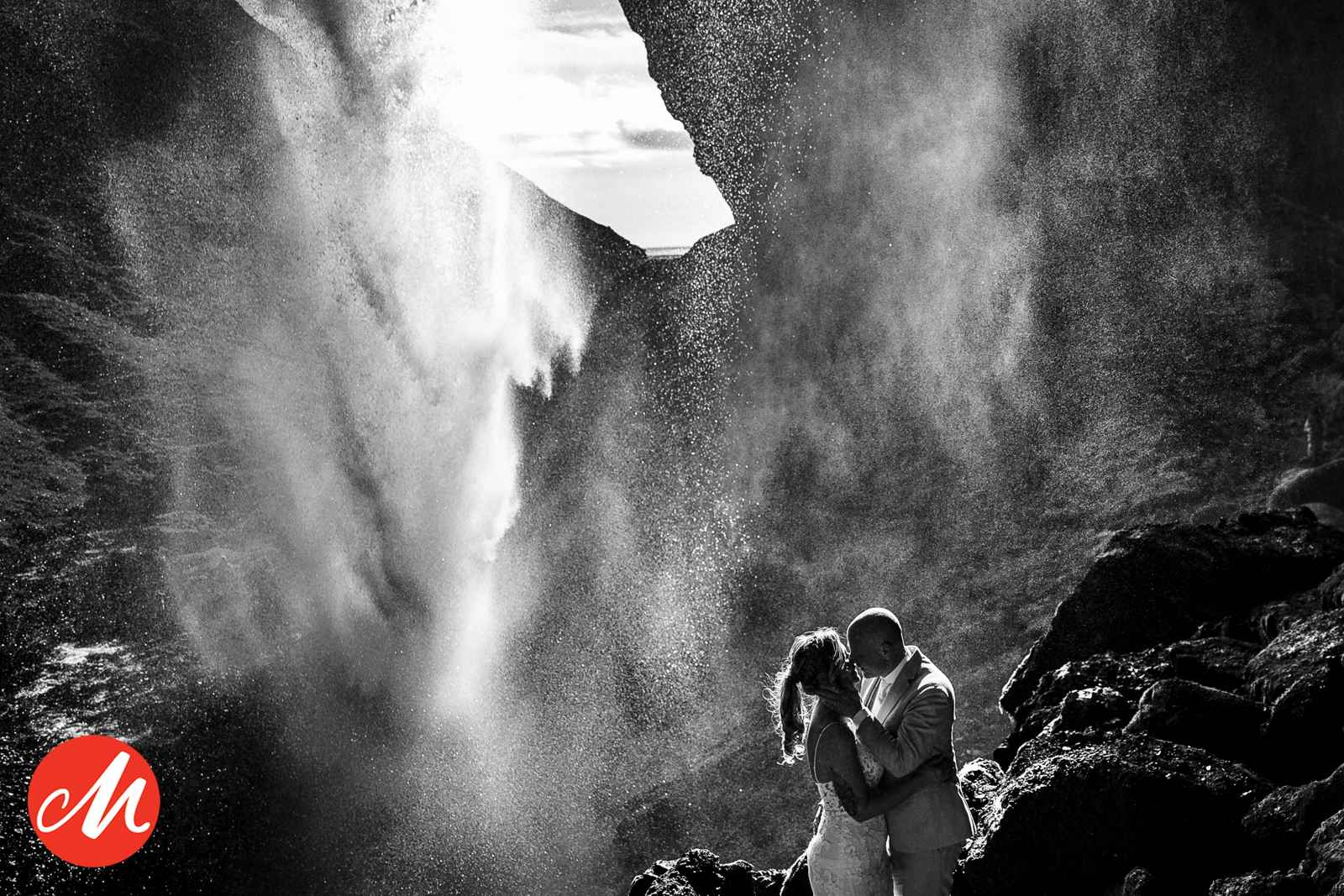 Sprookjesachtige zwart-wit foto van een bruidspaar in silhouet achter een krachtige waterval in IJsland.