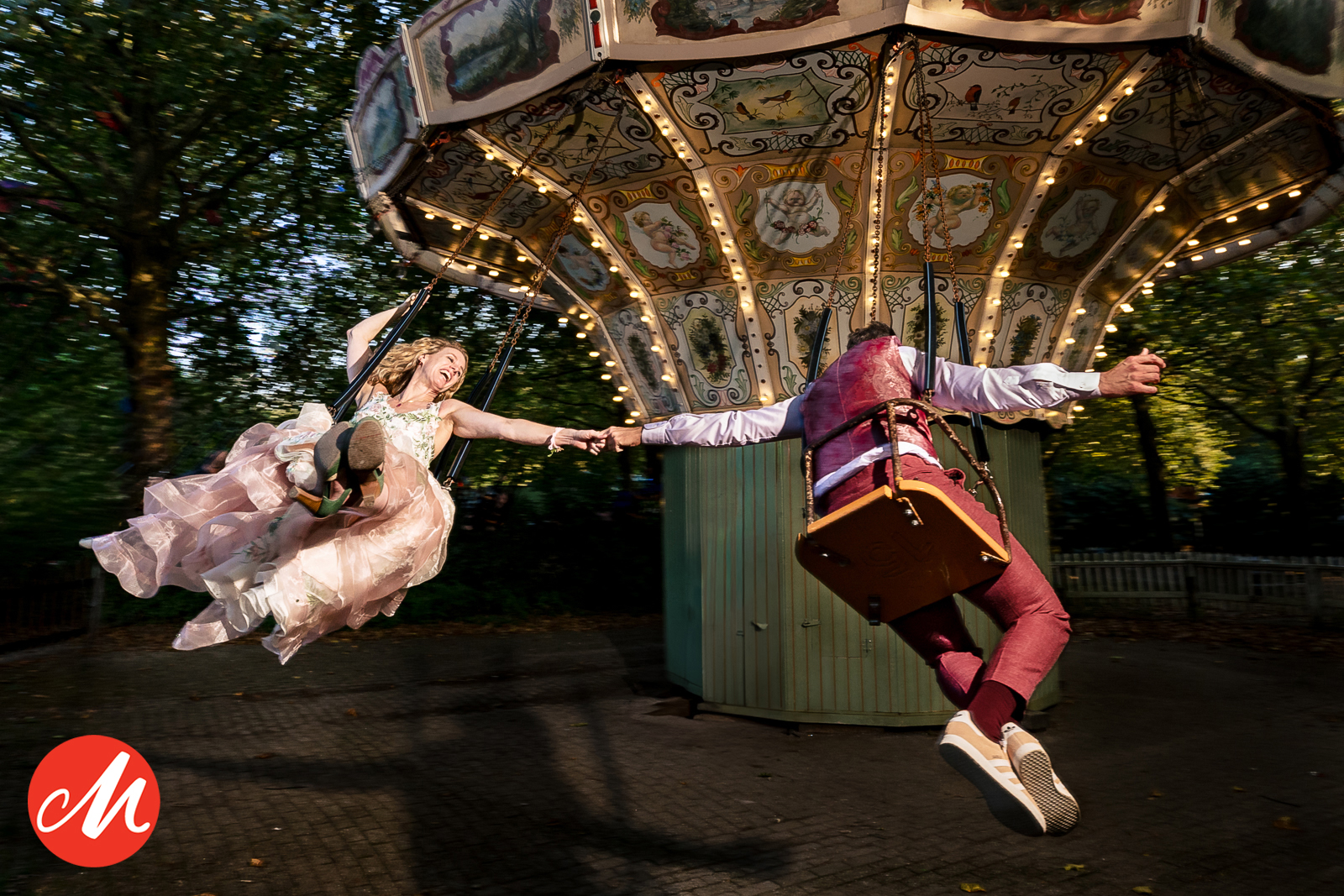 Kleurrijke actiefoto van een bruidspaar in een zweefmolen die elkaars hand vasthouden, creatieve bruidsfotografie Paco van Leeuwen.
