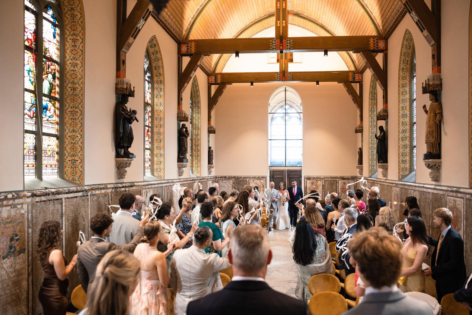 Bruid Nadine loopt arm in arm door het gangpad van de kapel tijdens de ceremonie