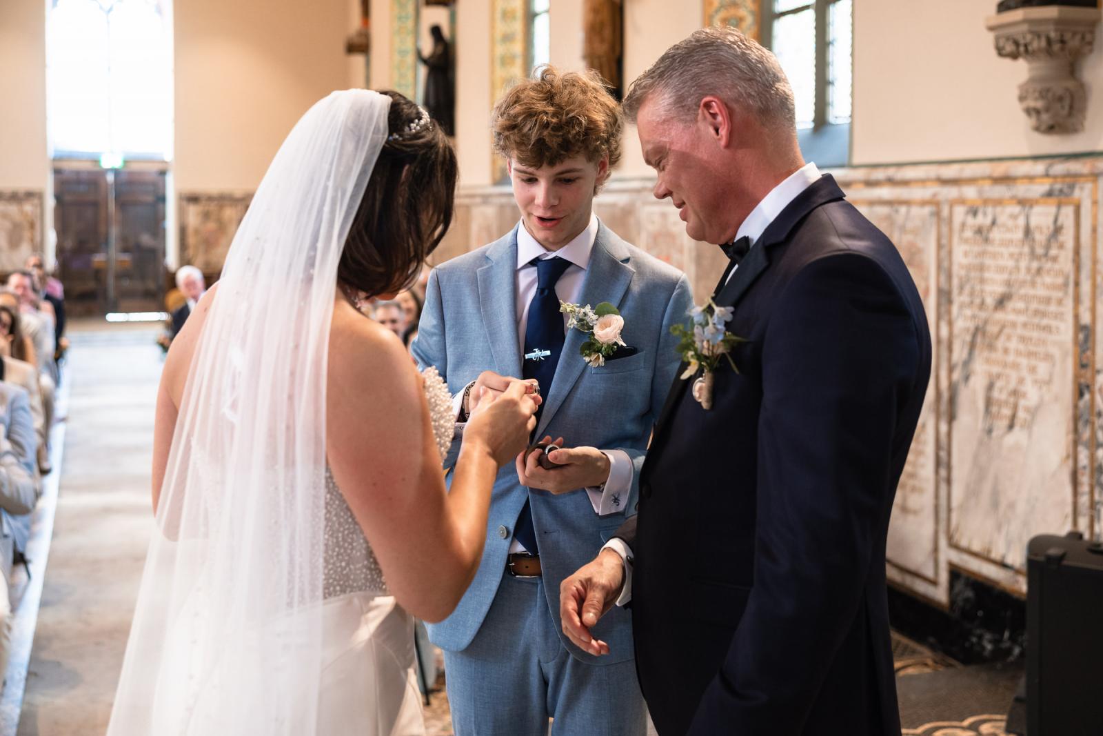 Bruidegom Mike schuift de trouwring aan de vinger van bruid Nadine waar de zoon bij staat na het brengen van de ringen
