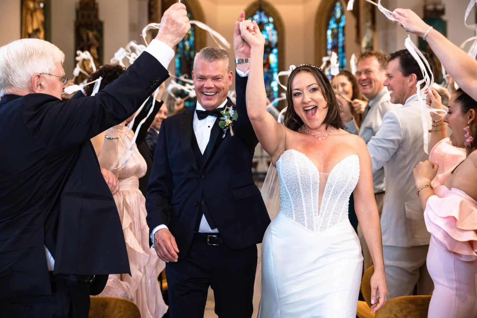 Bruid Nadine en bruidegom Mike lopen stralend door het gangpad onder applaus van gasten