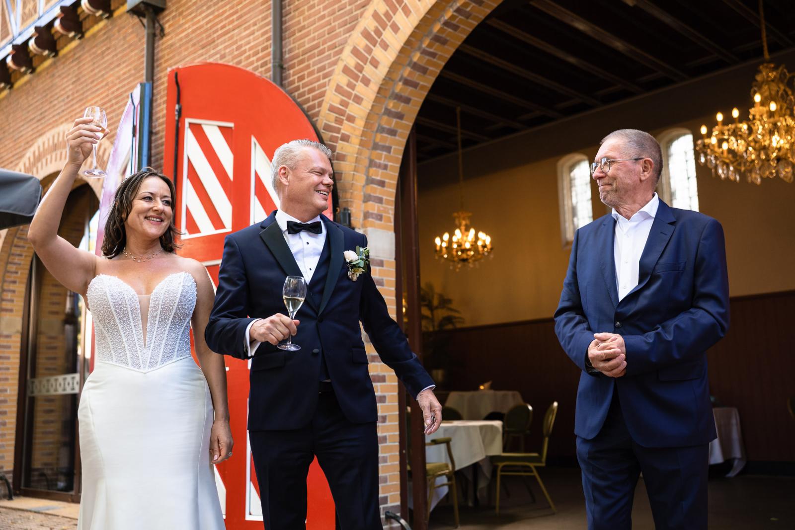 Bruidspaar Mike en Nadine heft proostend het glas bij de ingang van het Koetshuis van Kasteel de Haar.