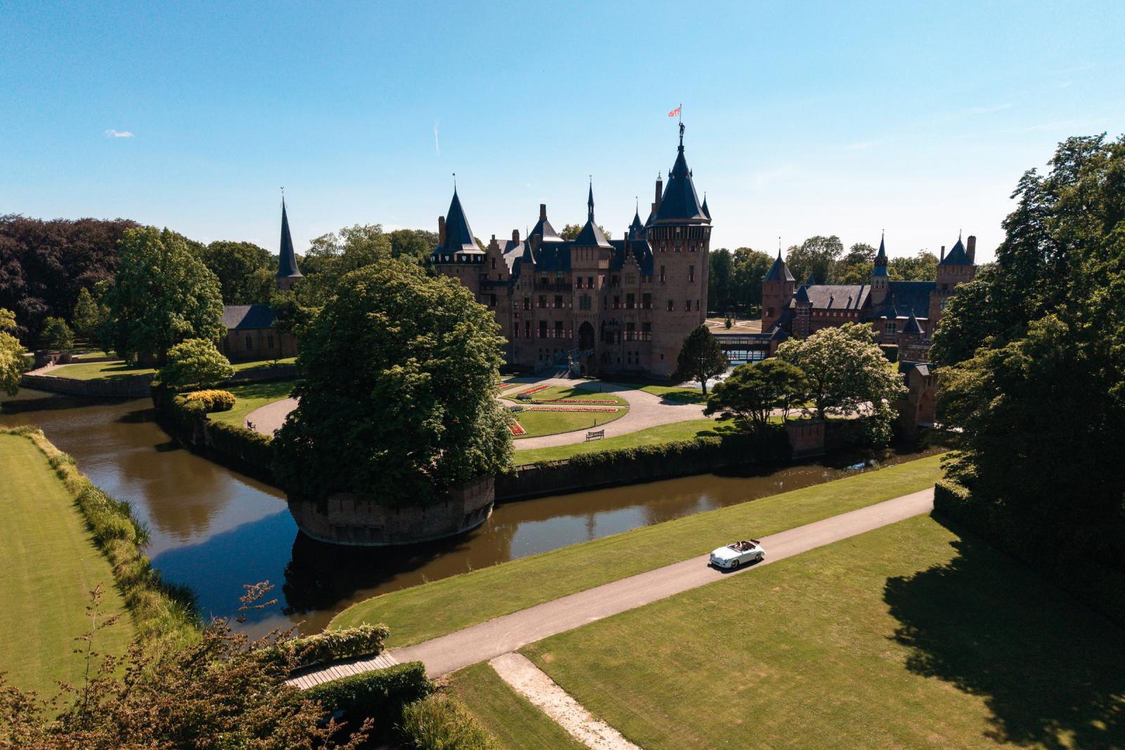 Dronefoto van Kasteel de Haar met de witte vintage Porsche van het bruidspaar rijdend over de oprijlaan.