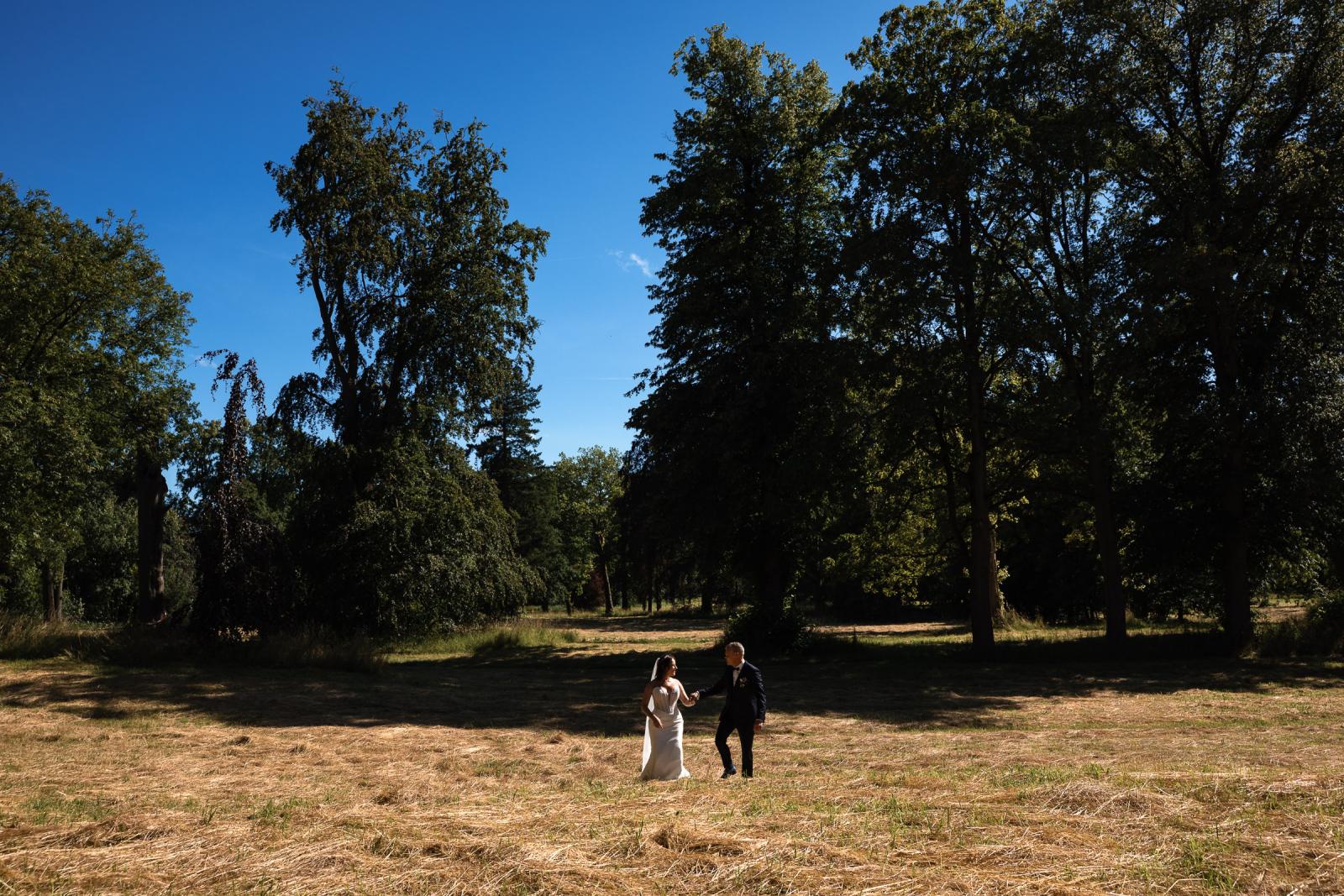 Bruidspaar Mike en Nadine wandelt hand in hand door een gemaaid grasveld in het park van Kasteel de Haar.