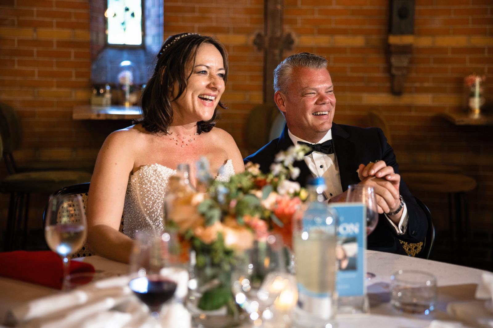 Bruid Nadine en bruidegom Mike lachen stralend aan de diner-tafel tijdens het huwelijksdiner om speech van de kinderen