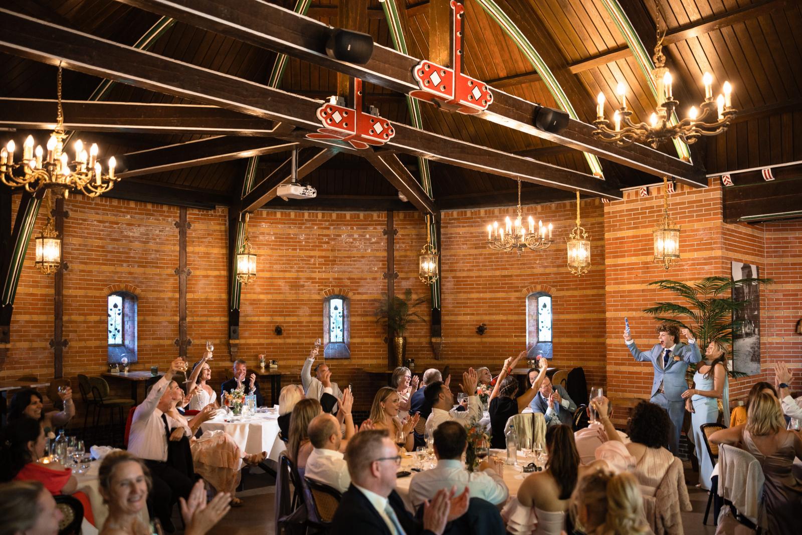 Sfeervol overzicht van de dinerzaal in Kasteel de Haar waar gasten heffen het glas op het bruidspaar.